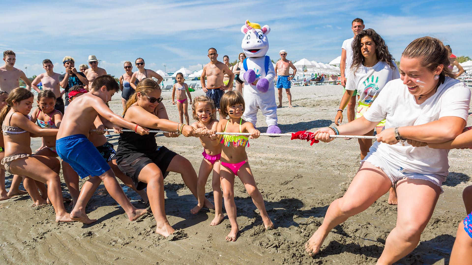 Strand-Seilziehen mit Begeisterung und einem riesigen Einhorn-Maskottchen.