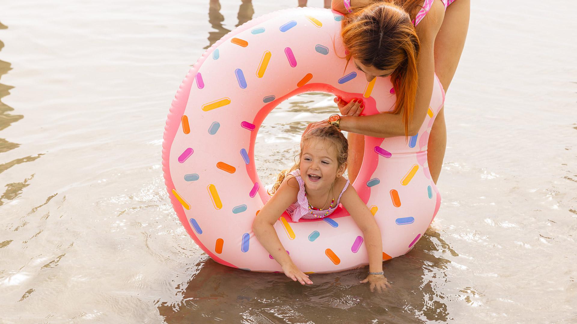 Bambina felice gioca in acqua con ciambella colorata.