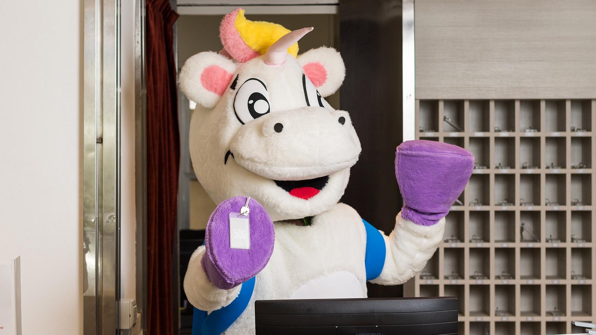 Ein fröhliches Einhorn begrüßt begeistert an der Hotelrezeption.