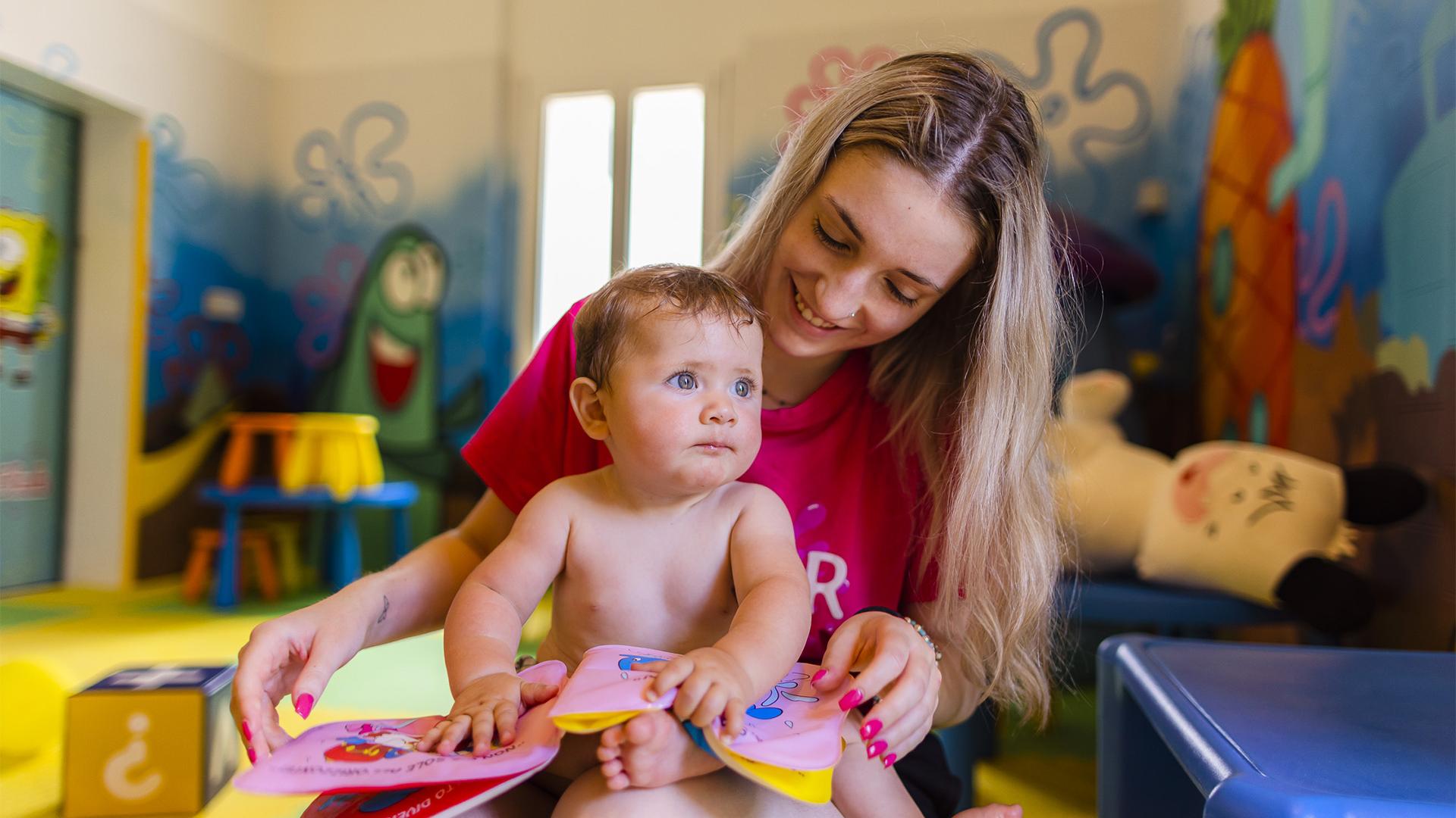 Bambino con braccioli arancioni vicino a piscina, ombrelloni colorati sullo sfondo.