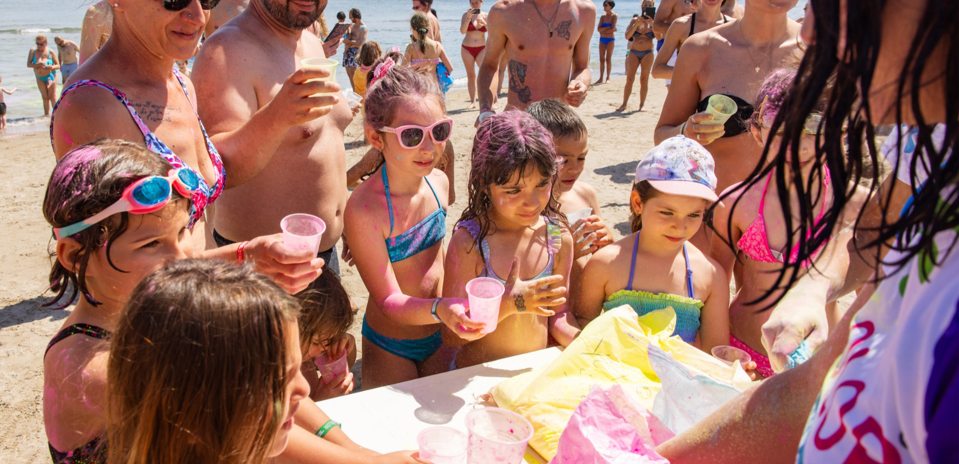 Fröhliche, bunte Kinder spielen am sonnigen Strand mit lächelnden Erwachsenen.