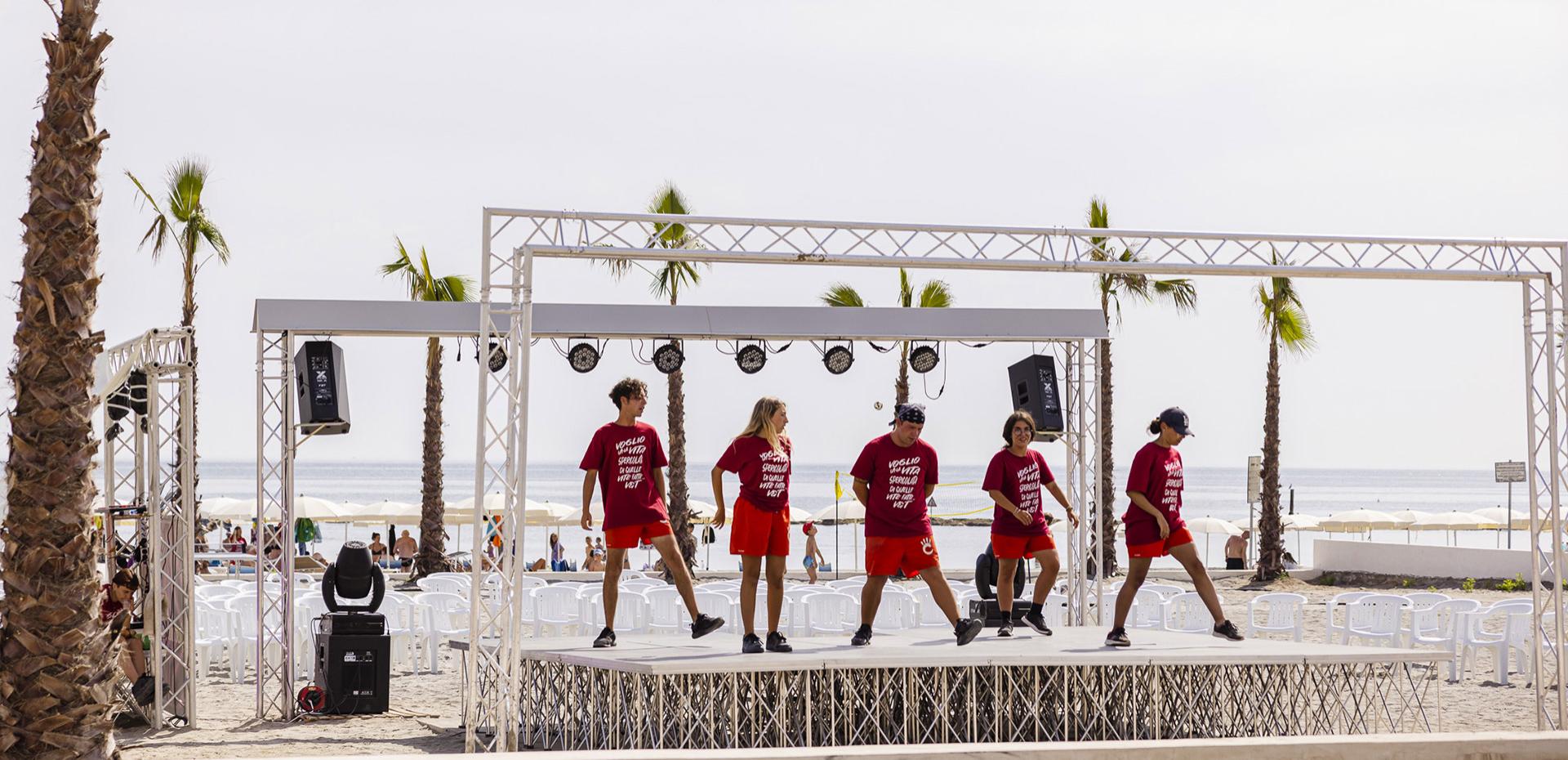 Junge Leute tanzen auf einer Strandbühne, sommerliche Stimmung und Freude.