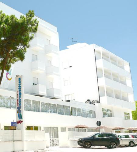 Hôtel blanc moderne, arbres, ciel bleu, ambiance relaxante et accueillante.