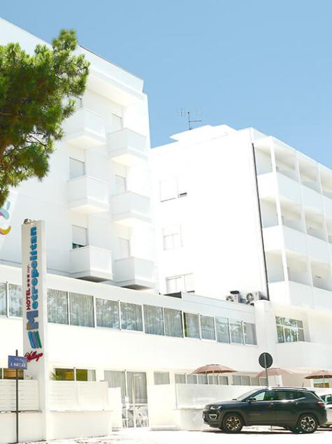 Hôtel blanc moderne, arbres, ciel bleu, ambiance relaxante et accueillante.