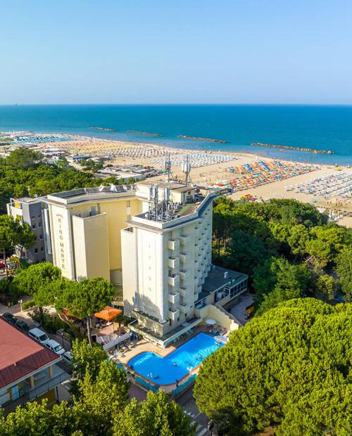 Vista aerea di un hotel con piscina vicino al mare e spiaggia affollata.