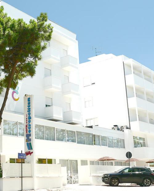 Hotel bianco moderno, alberi, cielo azzurro, atmosfera rilassante e accogliente.