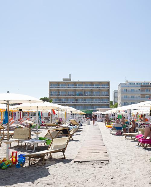 Spiaggia affollata, ombrelloni colorati, sole splendente, relax estivo.
