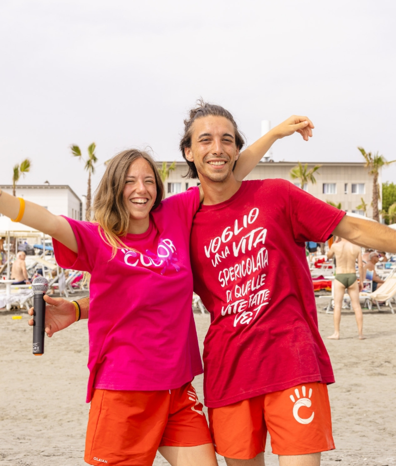 Zwei lächelnde Menschen am Strand, tragen bunte T-Shirts, wirken fröhlich.