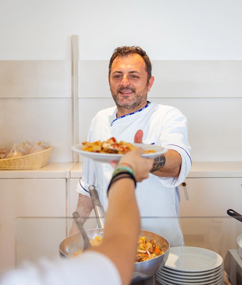 Lächelnder Koch serviert Pasta mit Wärme und Leidenschaft.